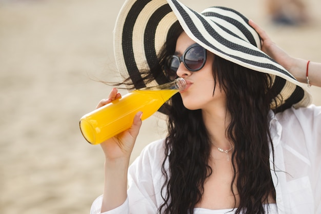 Pretty young woman drinking cocktail on the beach. Attractive girl offering a drink. Beautiful woman drinking lemonade