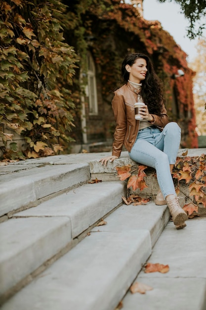 Pretty young woman drinking takeaway coffee at the outdoor stairs on autumn day