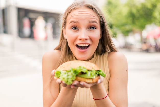 路上で屋外でハンバーガーを食べるかなり若い女性