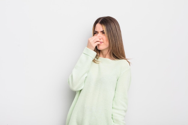 Pretty young woman feeling disgusted holding nose to avoid smelling a foul and unpleasant stench