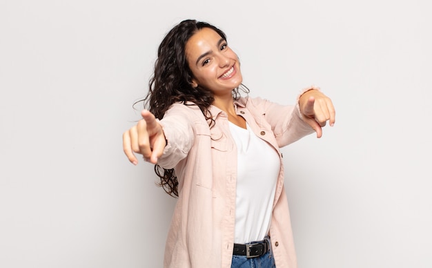 Bella giovane donna che si sente felice e sicura, indicando la telecamera con entrambe le mani e ridendo, scegliendo te