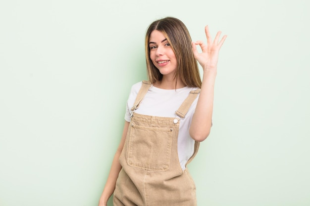 Pretty young woman feeling happy, relaxed and satisfied, showing approval with okay gesture, smiling