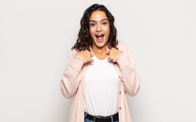 Pretty young woman feeling happy, surprised and proud, pointing to self with an excited, amazed look