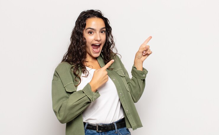Photo pretty young woman feeling joyful and surprised, smiling with a shocked expression and pointing to the side