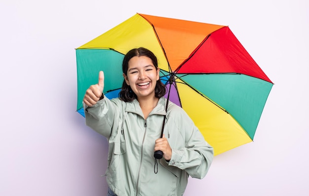 かなり若い女性が誇りを感じ、親指を立てて前向きに笑っています。雨と傘のコンセプト