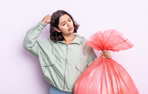 かなり若い女性は、頭をかいて、戸惑い、混乱していると感じています。ゴミ袋のコンセプト