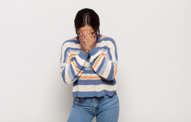 Pretty young woman feeling sad, frustrated, nervous and depressed, covering face with both hands, crying