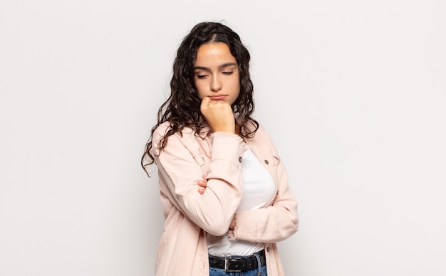 Pretty young woman feeling serious, thoughtful and concerned, staring sideways with hand pressed against chin