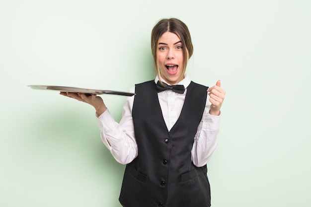 Pretty young woman feeling shockedlaughing and celebrating success waiter with a tray concept