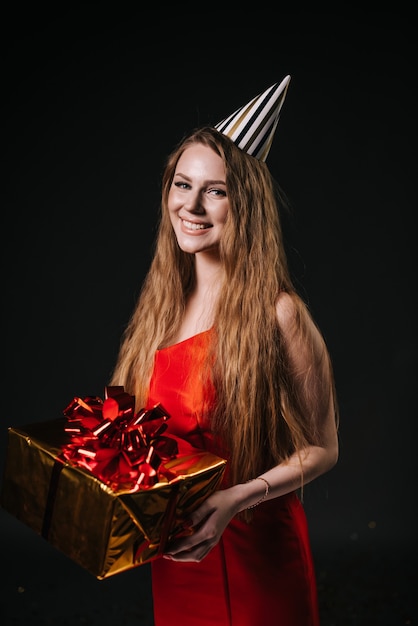 Pretty young woman in a festive cap holds a holiday box with a gift