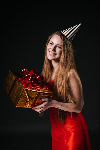 Pretty young woman in a festive cap holds a holiday box with a gift