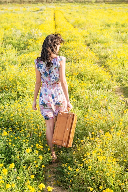 Pretty young woman in a field with a old suitcase