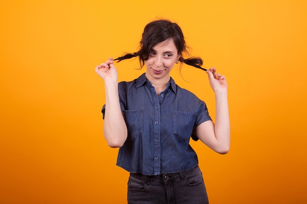 Pretty young woman happy about her hair style in studio over yellow background. Attractive caucasian woman with funky coiffure.