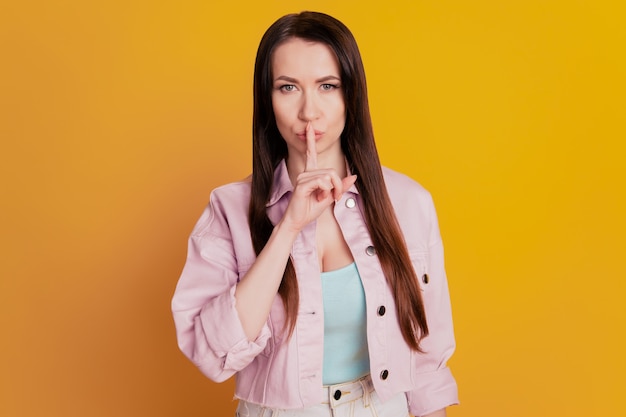 Pretty young woman hold finger lips show silence sign isolated on yellow background