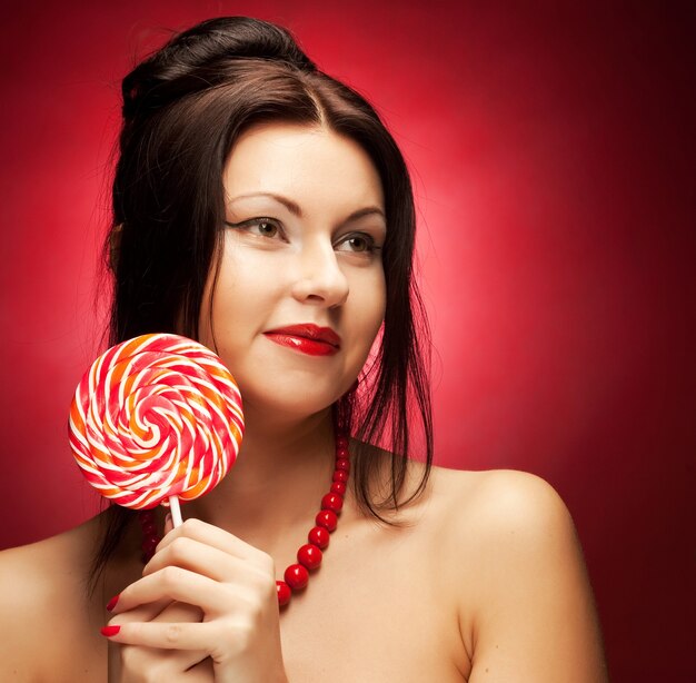 Piuttosto giovane donna con lecca lecca pop. su sfondo rosso.