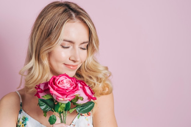 Pretty young woman holding pink roses in hand against pink background