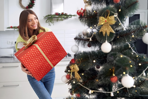 Pretty young woman holding wrapped red gift box at home