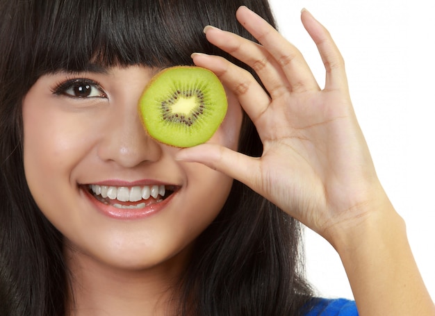 Pretty young woman holds kiwi in front of her eyes.