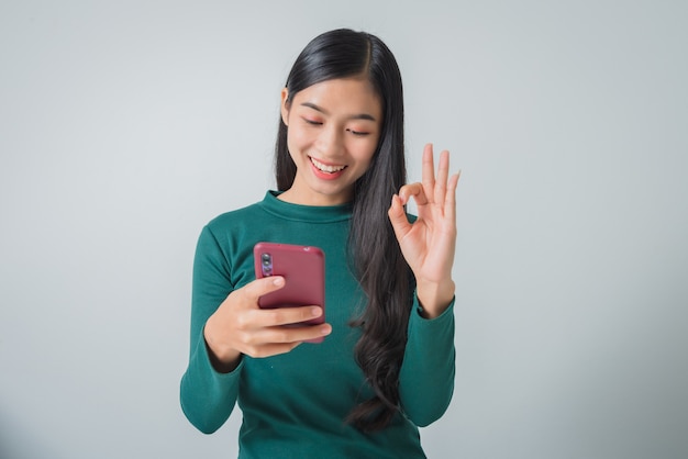 Pretty young woman holds smartphone and shows ok gesture