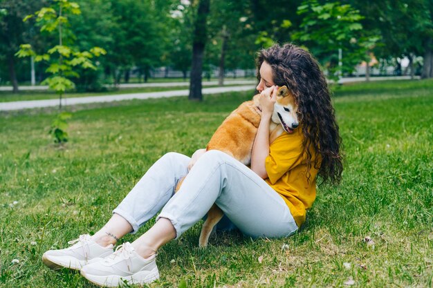 柴犬を抱きしめて、公園の芝生に座って笑っているかなり若い女性