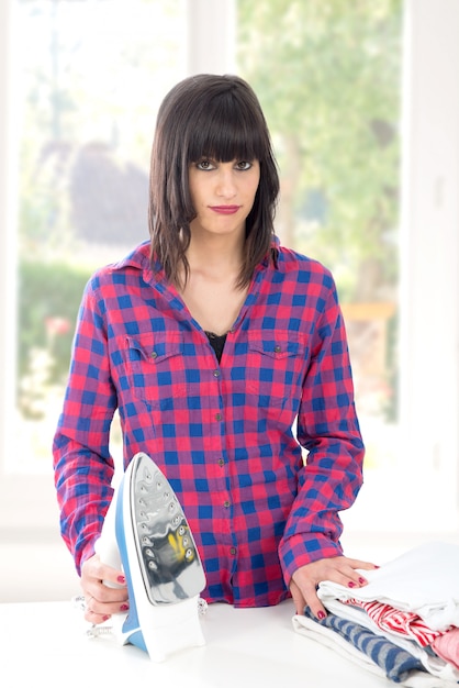 Photo pretty young woman ironing clothes on table