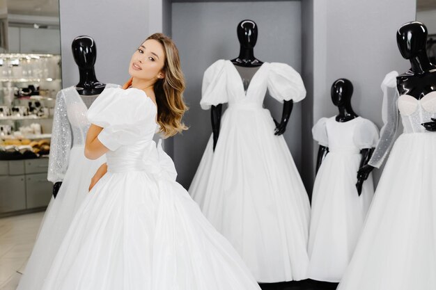 Pretty young woman is choosing a wedding dress in the shop The bridetobe is wearing a wedding dress for fitting