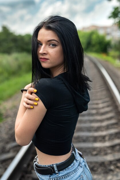 Pretty young woman is standing near the railway tracks, summer lifestyle