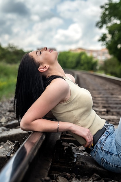 Bella giovane donna è in piedi vicino ai binari ferroviari, stile di vita estivo