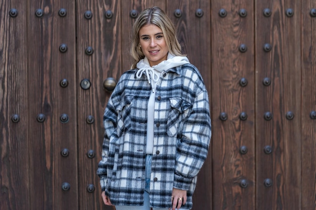 Pretty young woman in jeans and plaid jacket in front of a wooden door