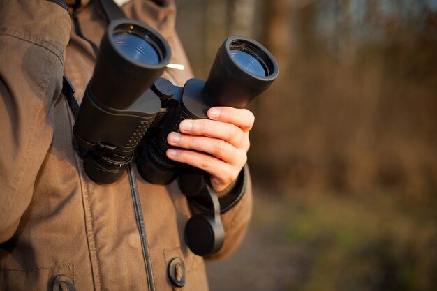 Pretty young woman looking after some animals by black binoculars in huge nature reservation; ornithology science