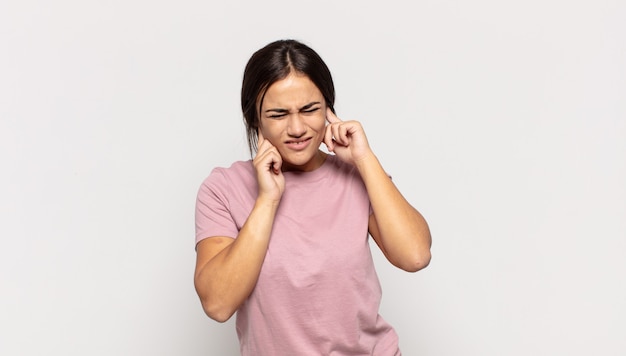 Bella giovane donna che sembra arrabbiata, stressata e infastidita, coprendo entrambe le orecchie per un rumore assordante, suono o musica ad alto volume