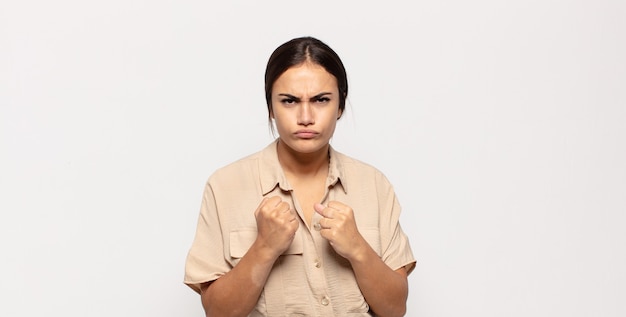 Pretty young woman looking confident, angry, strong and aggressive, with fists ready to fight in boxing position