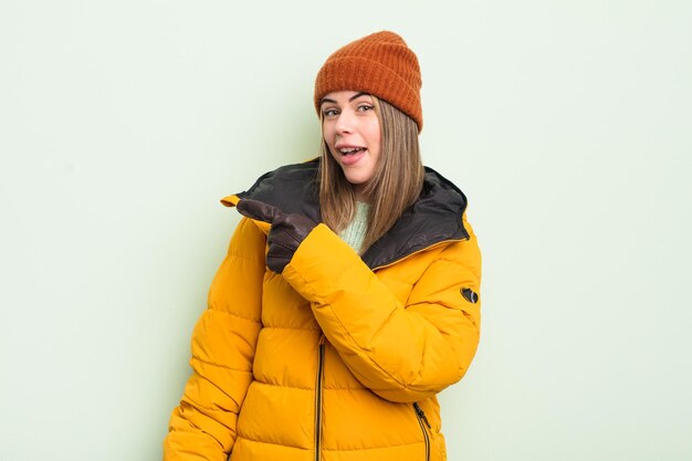 Pretty young woman looking excited and surprised pointing to the side cold weather concept