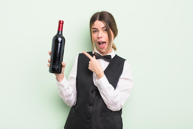 pretty young woman looking excited and surprised pointing to the side. waiter and wine bottle concept