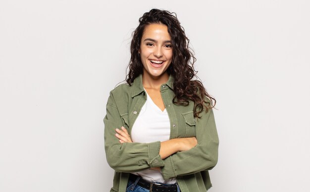 Pretty young woman looking like a happy, proud and satisfied achiever smiling with arms crossed