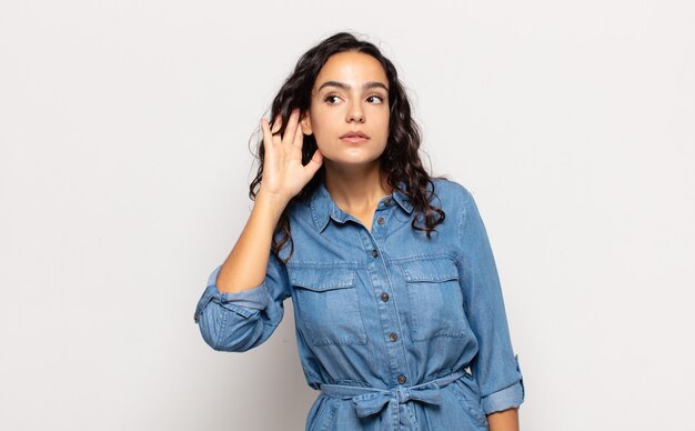 pretty young woman looking serious and curious, listening, trying to hear a secret conversation or gossip, eavesdropping