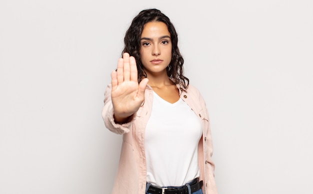 Pretty young woman looking serious, stern, displeased and angry showing open palm making stop gesture