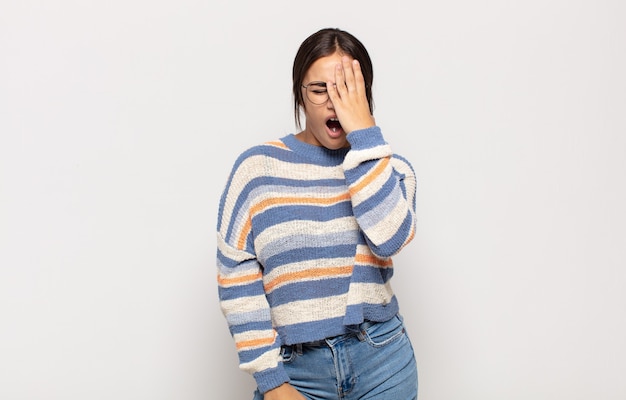 Pretty young woman looking sleepy, bored and yawning, with a headache and one hand covering half the face