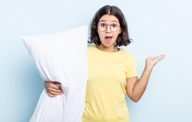 Pretty young woman looking surprised and shocked, with jaw dropped holding an object. bed concept