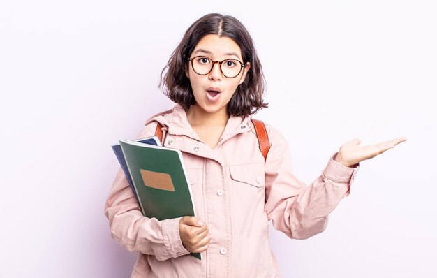 Pretty young woman looking surprised and shocked, with jaw dropped holding an object. student with books concept