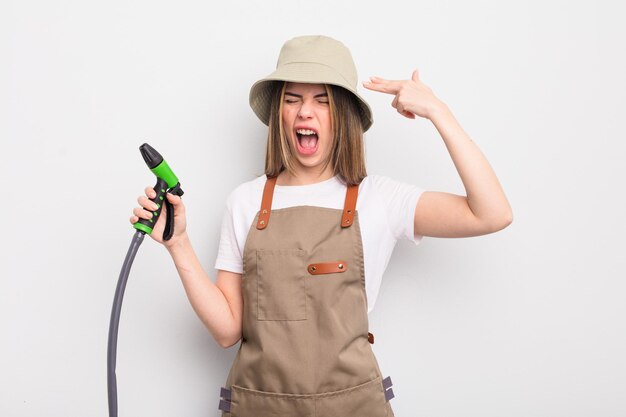 Pretty young woman looking unhappy and stressed suicide gesture making gun sign gardener watering concept