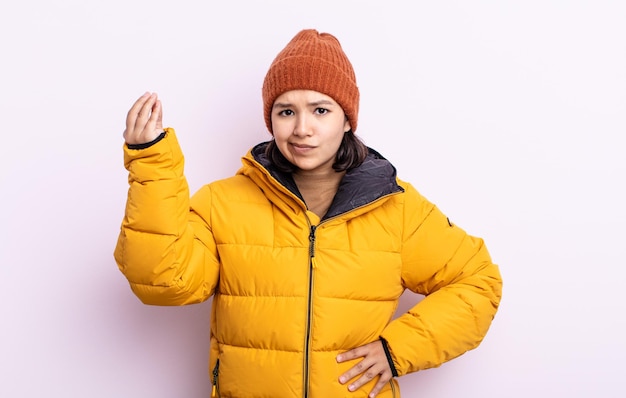 pretty young woman making capice or money gesture, telling you to pay. cold weather concept