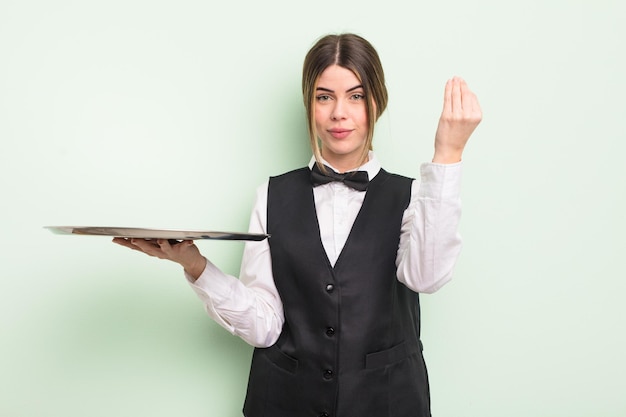 Pretty young woman making capice or money gesture, telling you to pay. waiter with a tray concept