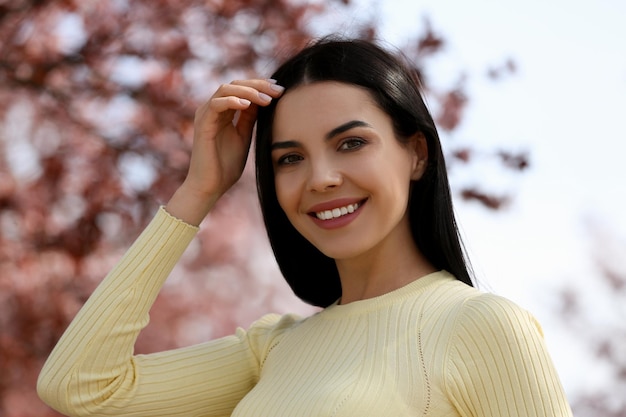 Pretty young woman near beautiful blossoming trees outdoors Stylish spring look