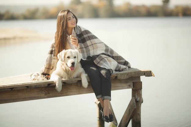 Pretty young woman outdoors with dog. Golden retriever and his owner resting near the water and drinking tea