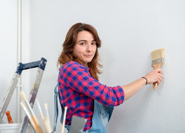 Pretty young woman painting wall white color