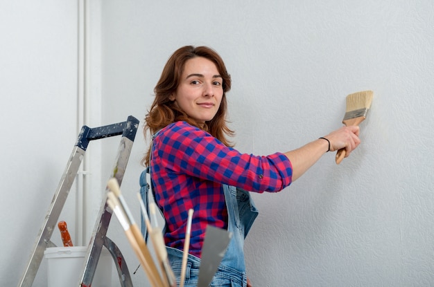 Pretty young woman paints the wall white color