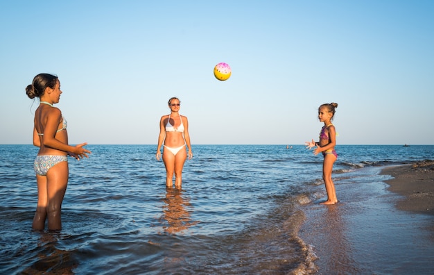 Pretty young woman plays ball with her charming daughters on the sea shore