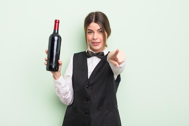 Pretty young woman pointing at camera choosing you. waiter and wine bottle concept