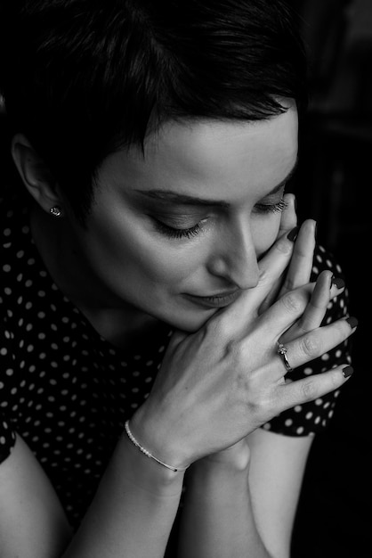 Pretty young woman portrait with her clasped fingers hands close to face, black and white styled